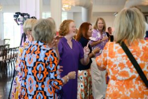 A young woman in a purple dress laughs while surrounded by other women.