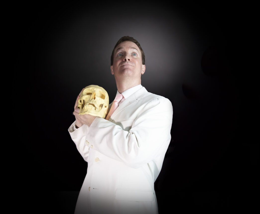 A man in a white suit holds a skull