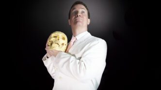 A man in a white suit holds a skull