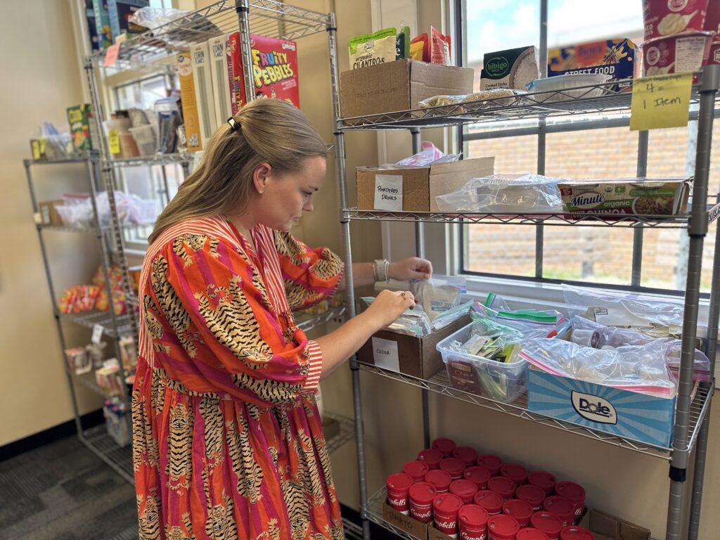 Abby Morningstar, wearing an orange dress with tigers on it, looks at a food item on a wire shelf in the Nook.