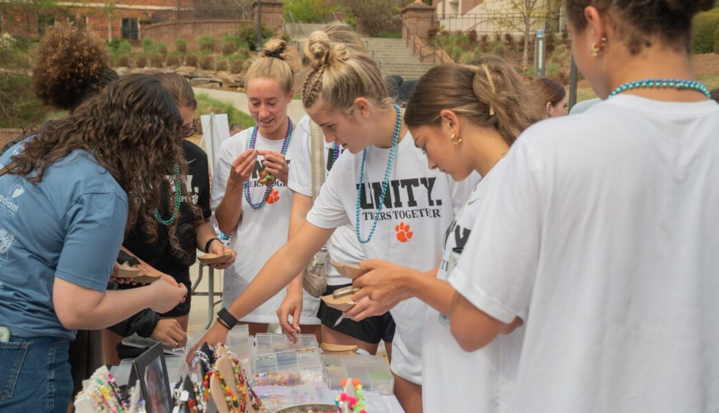 students gather around a table and make necklaces with beads in support of suicide prevention at the Out of the Darkness Campus Walk