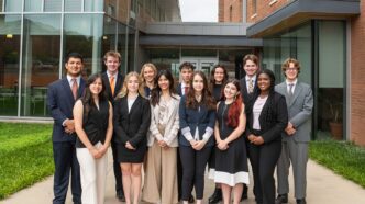 A group of 13 students starting their first semester in one of Clemson's two premier scholarship programs standing and posing together in front of the Honors Center on Clemson University campus.