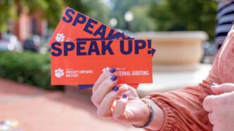 A hand with purple painted fingernails holding a bookmark that reads SPEAK UP!