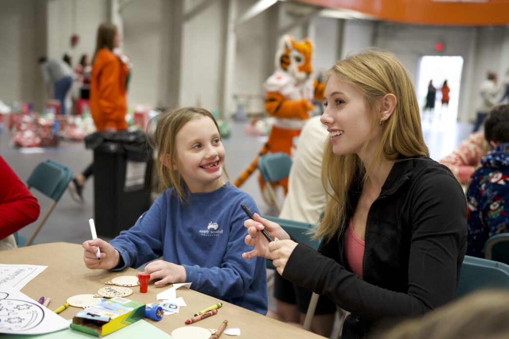 A student volunteer smiles while working with an elementary school child at Christmas 4 Kids on Clemson's campus