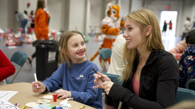 A student volunteer smiles while working with an elementary school child at Christmas 4 Kids on Clemson's campus