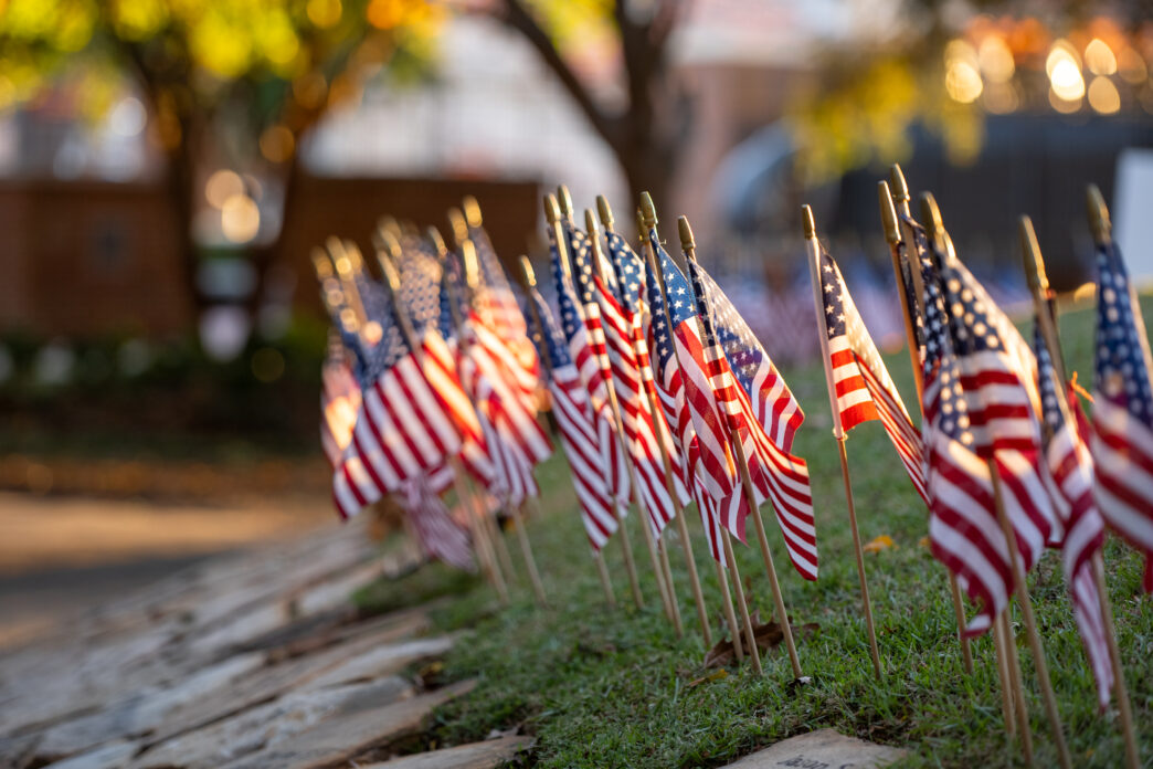 Small American flags are planted in the grass on the Scroll of Honor.