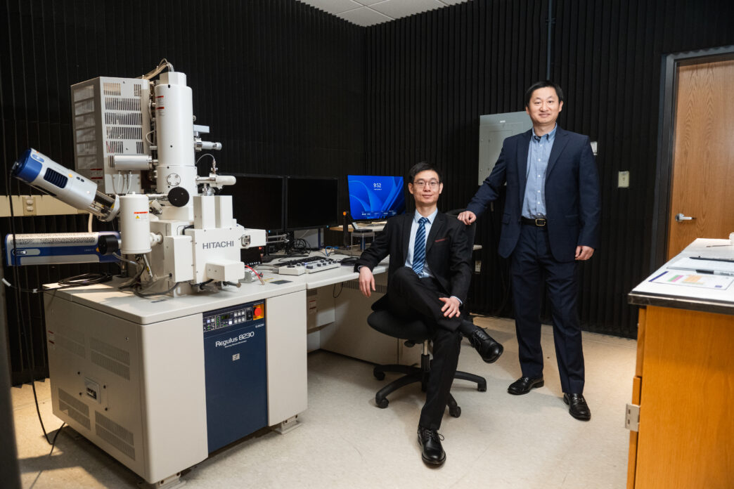 Two men sitting next to a large electron microscope