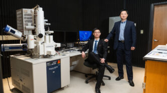 Two men sitting next to a large electron microscope