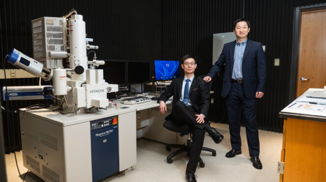 Two men sitting next to a large electron microscope