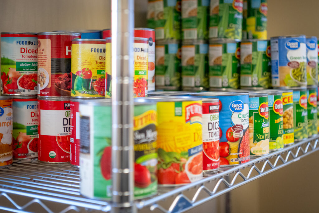 Canned vegetables, including tomatoes and green beans, are stacked and lined up on wire shelves in The Nook.