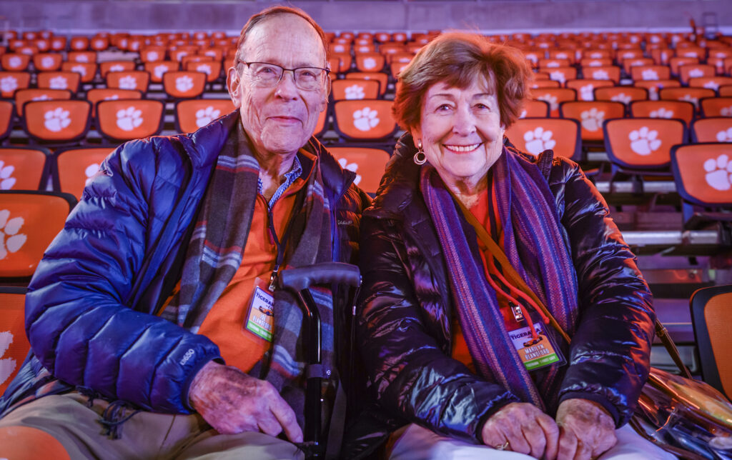 An older couple dressed in warm winter jackets sits in the stands of Memorial Stadium