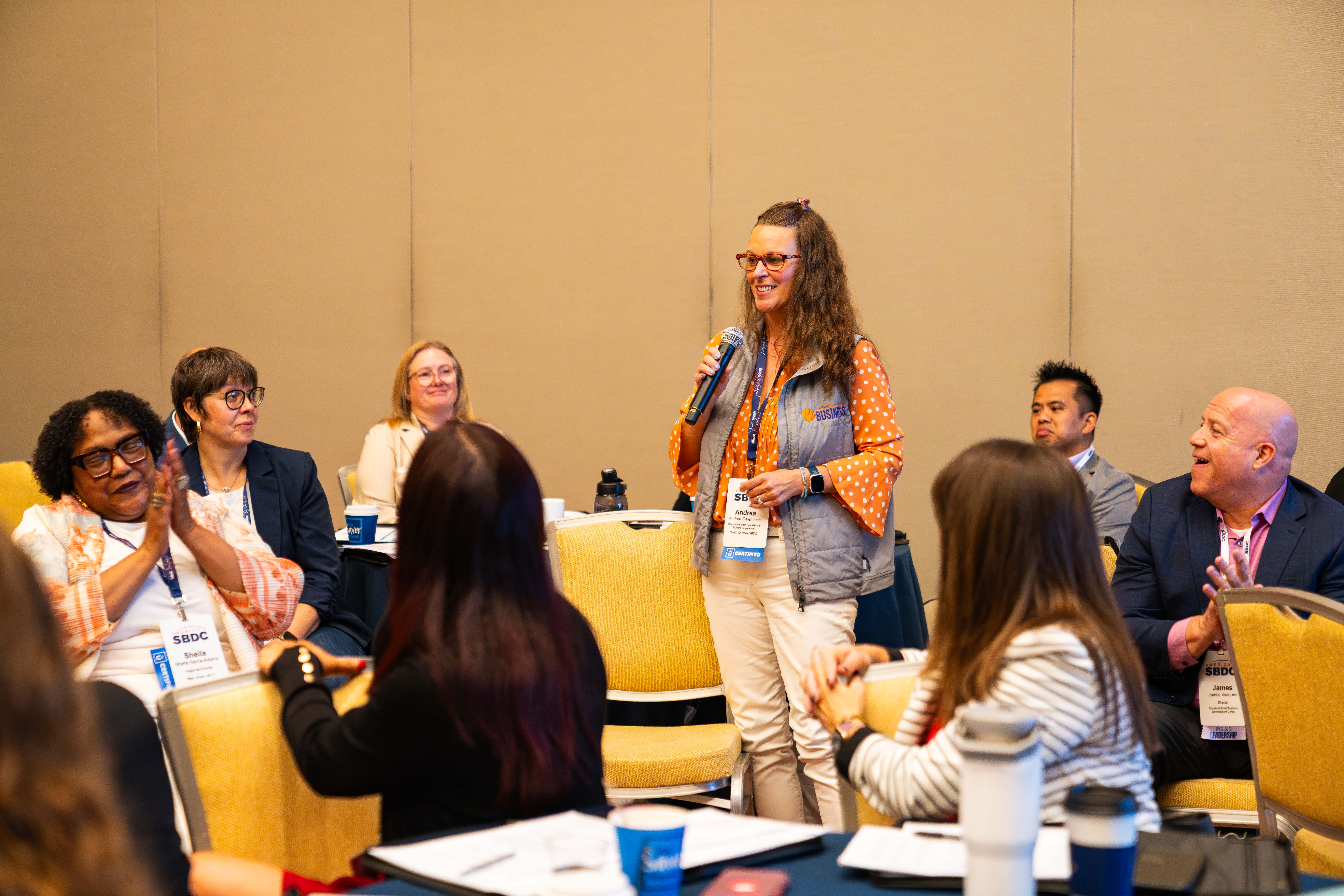 Andrea Galehouse with microphone talking to business group.