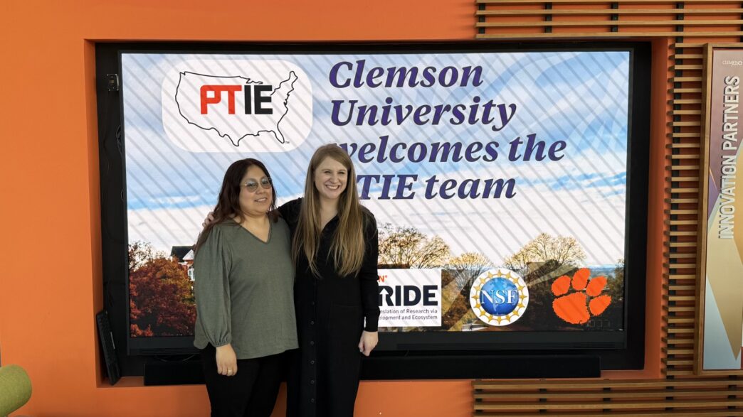 Two women stand in front of a screen that reads Clemson University welcomes PTIE team.