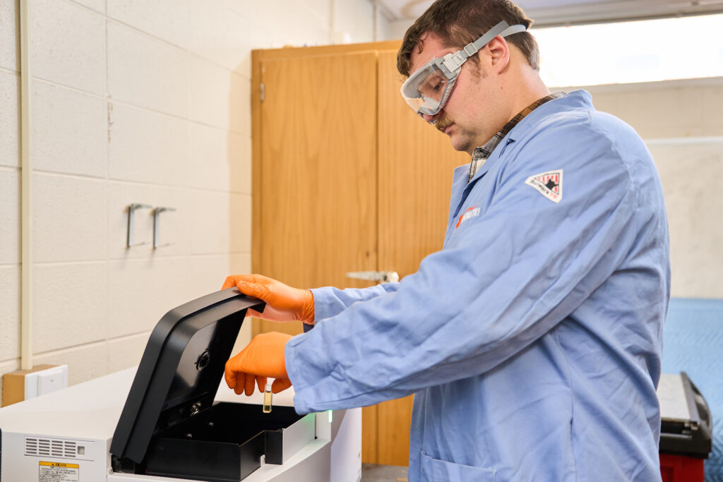 A man wearing a blue lab coat puts a test tube in a machine in a science lab at Clemson.