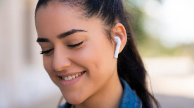 Portrait of young woman listening to music with earpods while standing outdoors on the street.