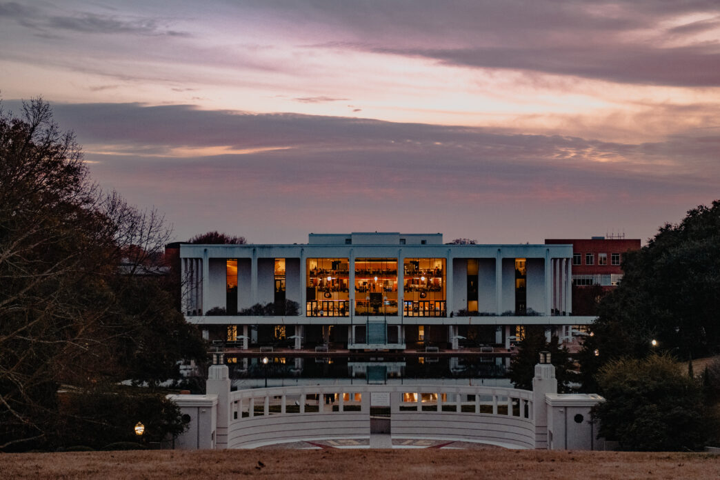Cooper Library sits in dusk behind the reflection pond from a distance.