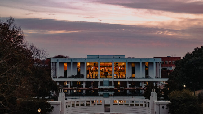 Cooper Library sits in dusk behind the reflection pond from a distance.