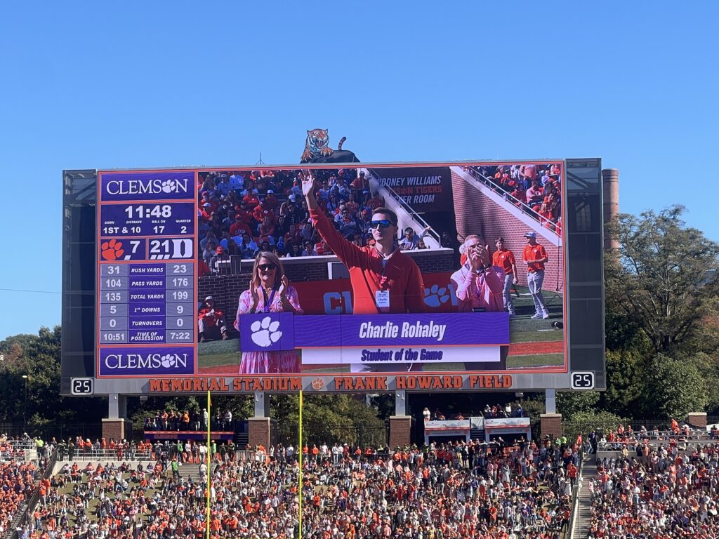 A student waving on a large screen at a football game