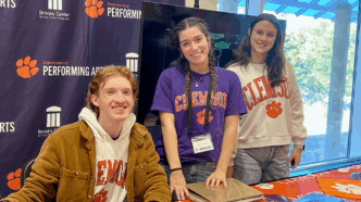 Three students wearing Clemson t-shirts smile for a photo in front of a Clemson Performing Arts backdrop