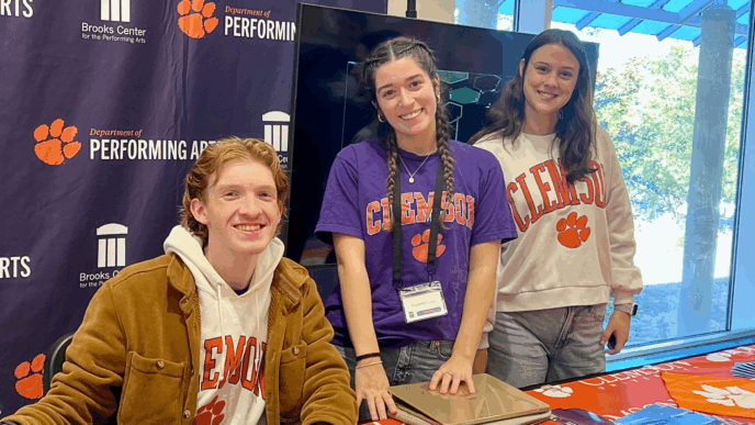 Three students wearing Clemson t-shirts smile for a photo in front of a Clemson Performing Arts backdrop