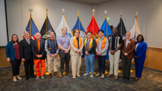 December 2025 graduates and Clemson University staff in front of American and military flags in Hendrix Student Center