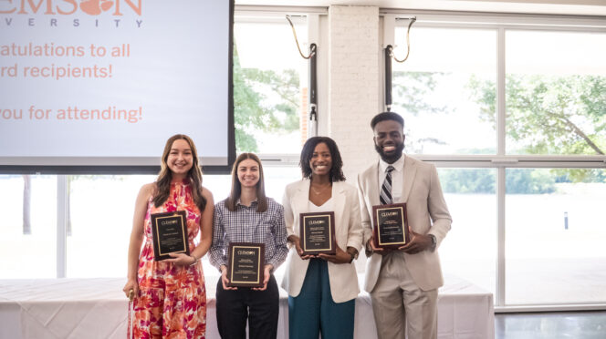 Four students in professional attire hold awards from Clemson University
