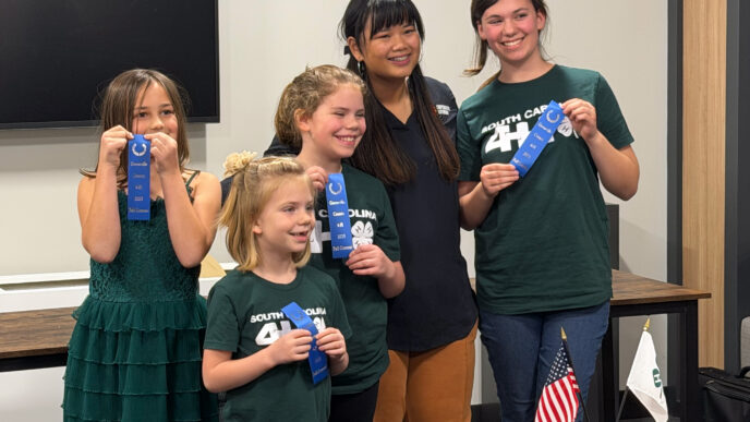 A group of young girls wear matching forest green t-shirts and hold blue ribbons.