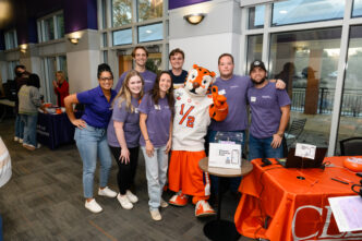 A group of individuals pose with the Tiger mascot inside a building on Clemson's campus