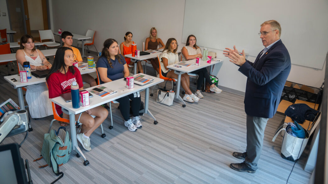 A man in a suit speaks in front of students within a classroom