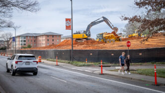 A construction crew clears an opening next to buildings adjacent to a highway on Clemson University's main campus