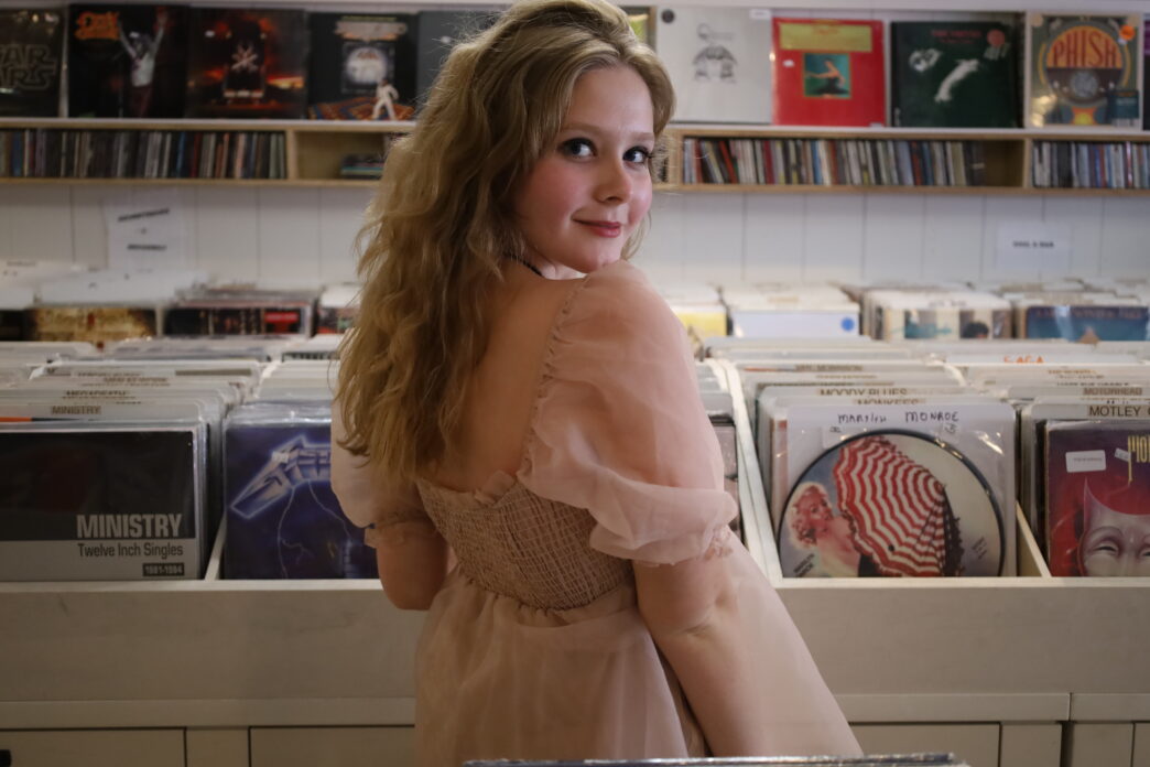 Caroline Warner poses in front of a bin of vinyl records