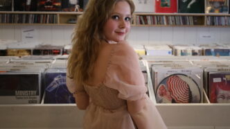 Caroline Warner poses in front of a bin of vinyl records