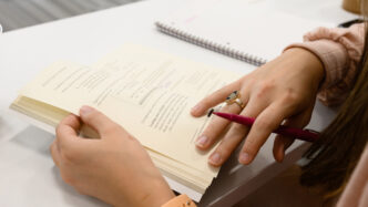 A student wearing a Clemson Ring and holding a pen opens a book for class.