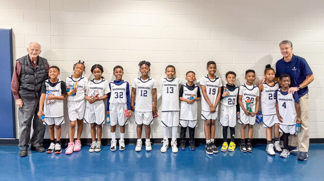 A youth basketball team lined up against a wall of a gym with their two coaches, the one on the right is Tony Perticone, a Clemson alumni who started the basketball program at Atlanta Youth Academy.