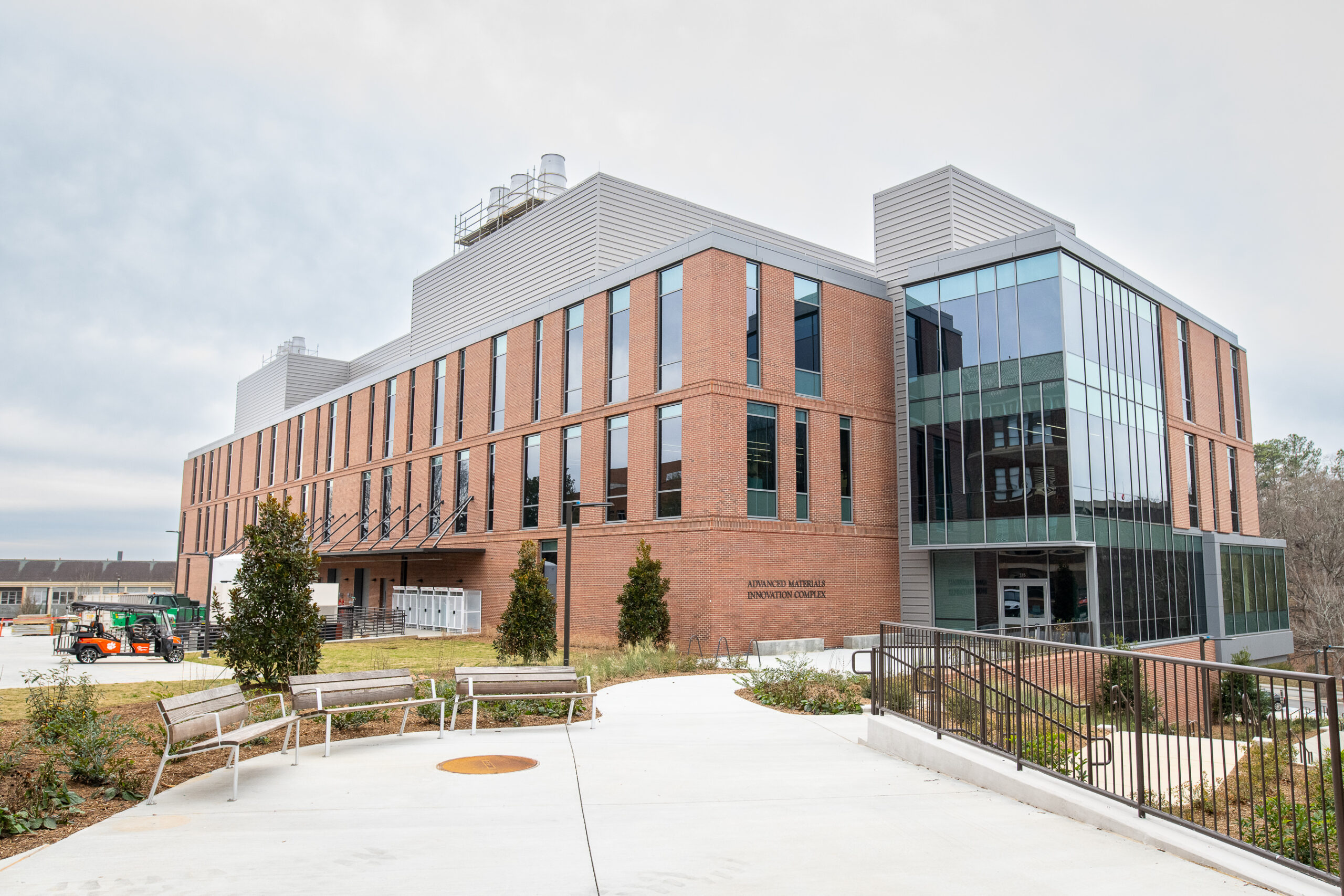A sidewalk leads to a modern four-story brick and glass building with large windows on one side.