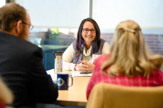 Three people chat and smile around a conference room table.