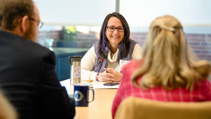 Three people chat and smile around a conference room table.