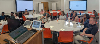 People sit at round tables while listening to a speaker.