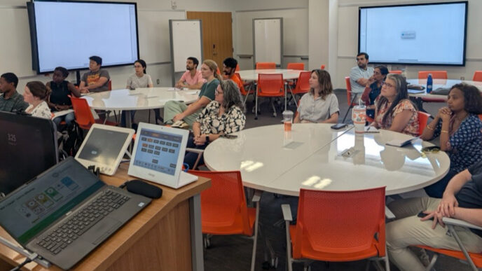 People sit at round tables while listening to a speaker.