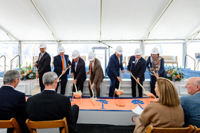 Individuals in suits dig shovels into sand for a ceremonial groundbreaking