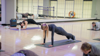 A fitness instructor leads a pilates class inside of a studio space