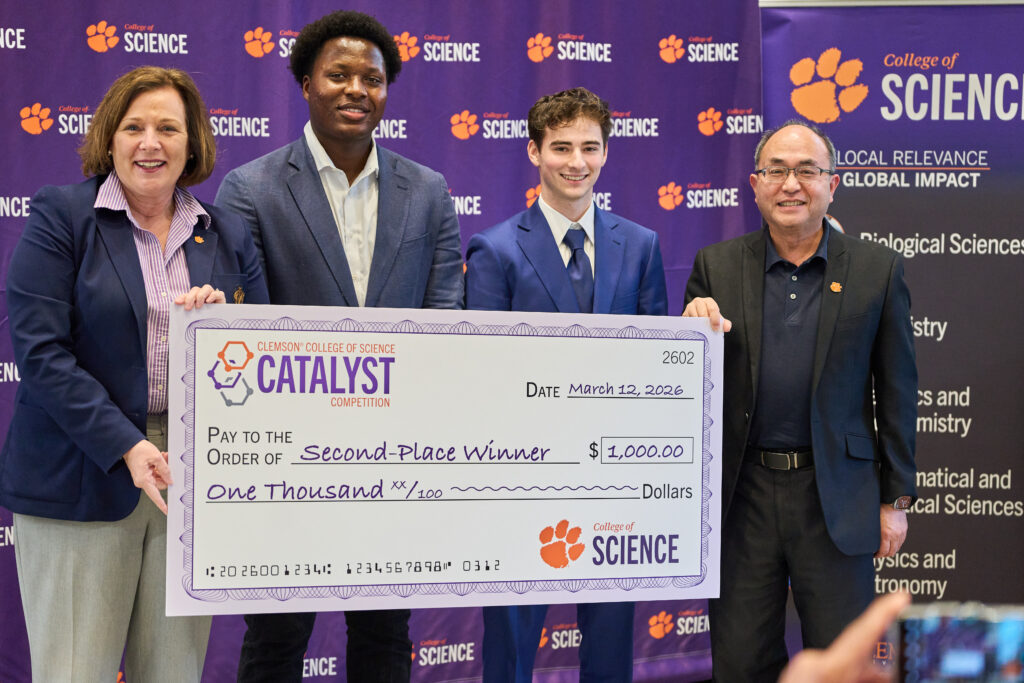 Two students, flanked by a woman and a man, hold a big check for second place in the Catalyst Competition .