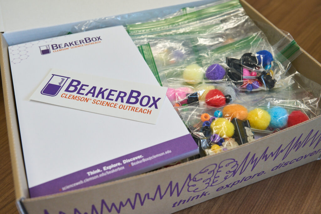 Ένα κουτί με αυτοκόλλητο Beaker Box και σημειωματάριο μαζί με μερικές χρωματιστές χάντρες και μινιατούρες "pom pots" που χρησιμοποιούνται για μαθήματα φυσικών επιστημών.