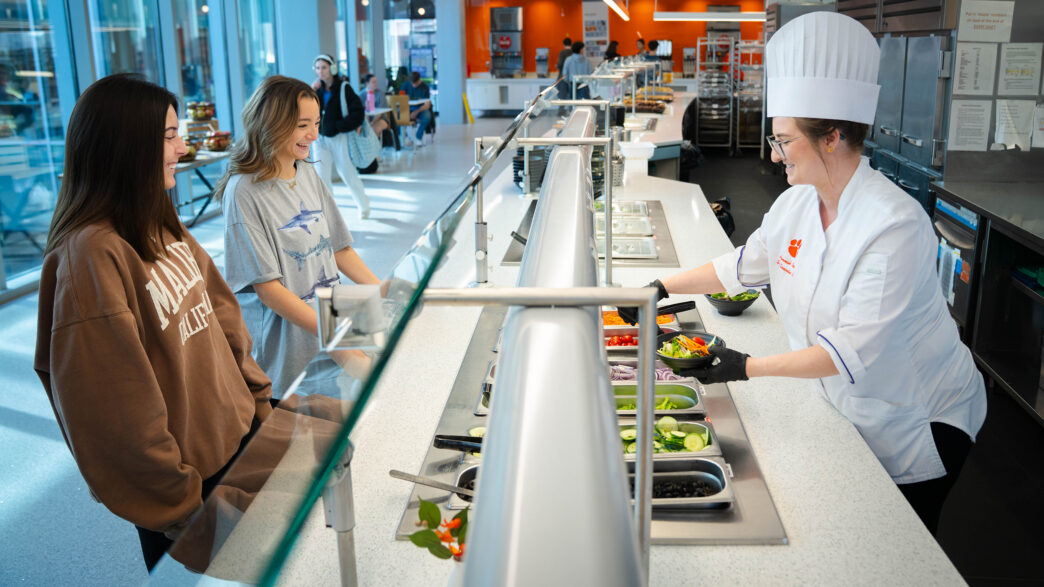 Students order a salad from a dining hall salad bar.