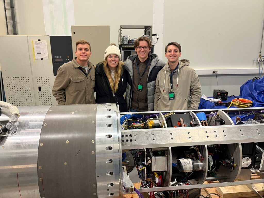 Four students stand in front of a sounding rocket on which their experiment was launched by NASA in Norway.