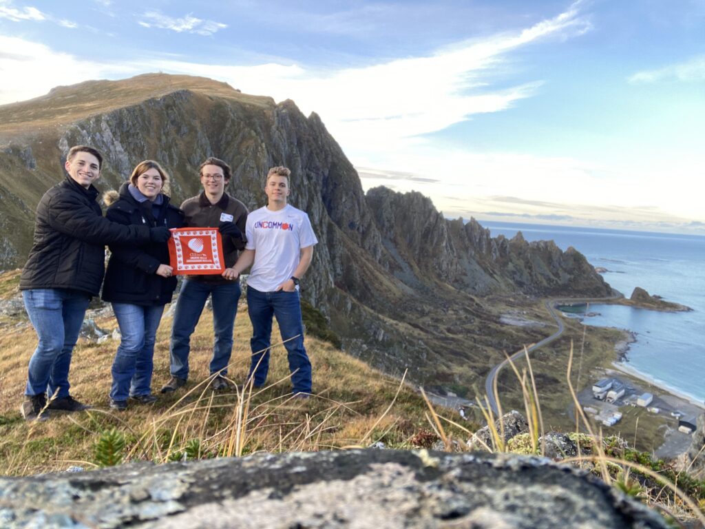 Four students - a woman and three men - hold a Tiger Paw rag on a mountain in Norway.