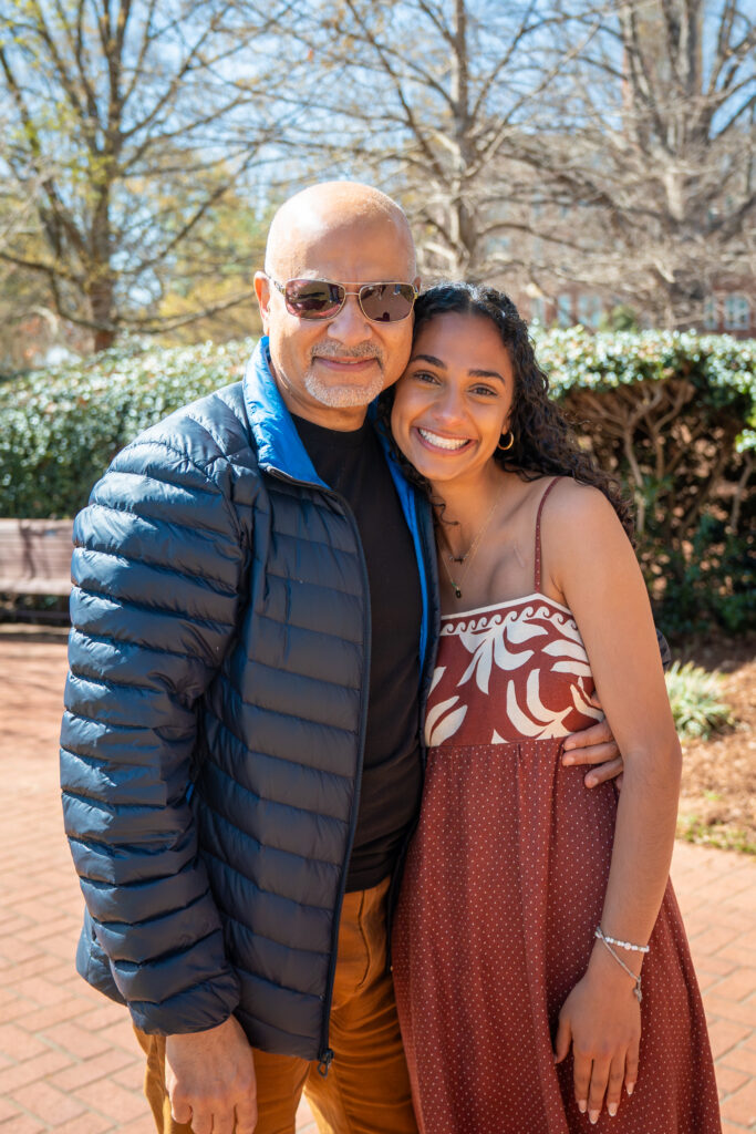 A male in a jacket hugs a female in a dress on main campus