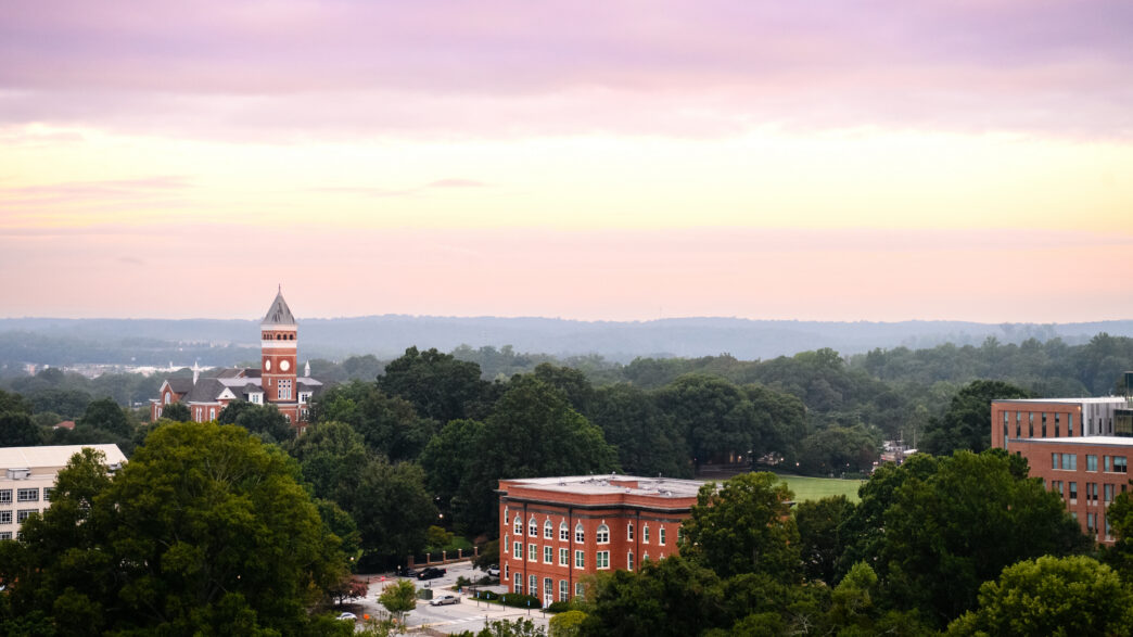 A sunrise over Clemson with Tillman Hall visible below orange and purple clouds.