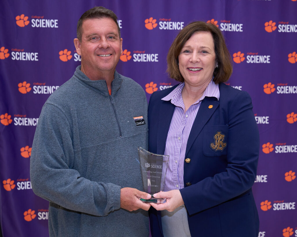 A man wearing a pullover stands next to a woman wearing a blue suit jacket. they are holding an acrylic trophy.