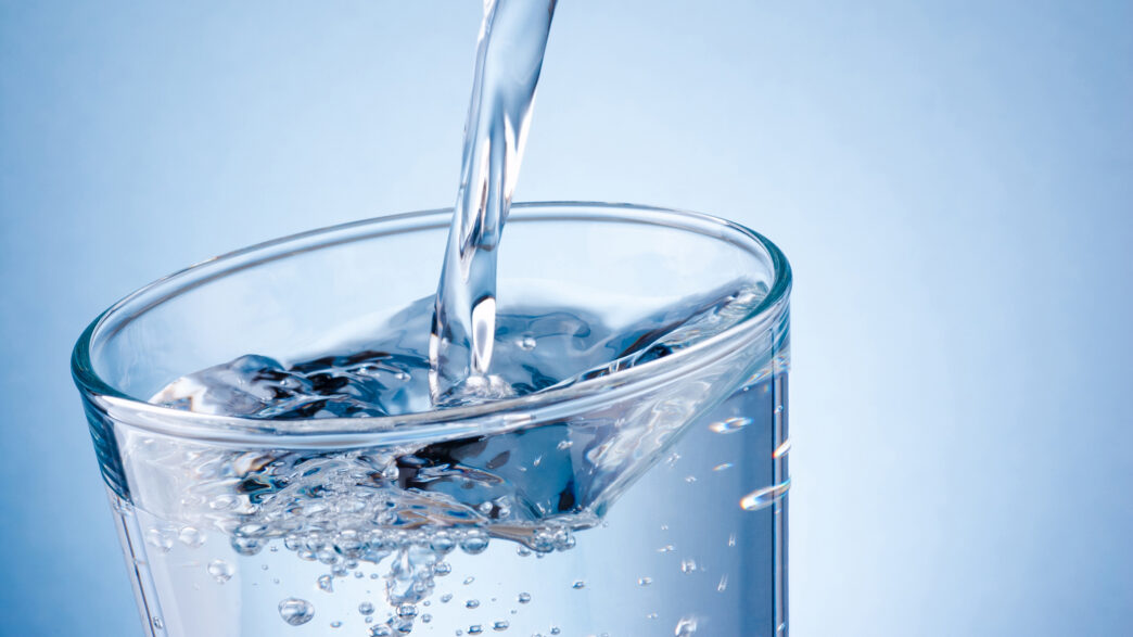 Pouring water into glass on a blue background